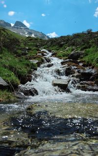 Scenic view of river flowing by mountain against sky