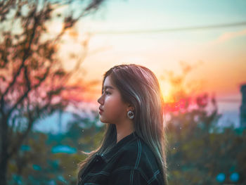 Portrait of young woman looking away against sky during sunset
