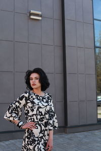 Fashionable young woman wearing floral patterned dress standing against building in city