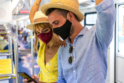 Smiling couple wearing mask using smart phone standing in bus