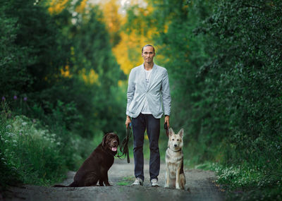 Portrait man standing with of dogs against trees