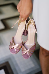 High angle of crop anonymous female standing with pair of elegant high heeled shoes on blurred background of floor in shop