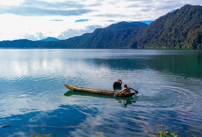 Young man in boat on lake against mountains