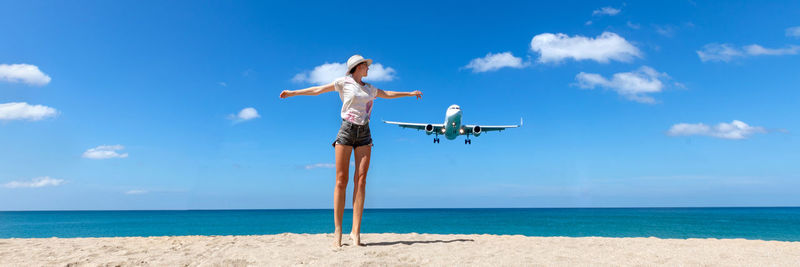 Girl looking at the flying plane above the sea