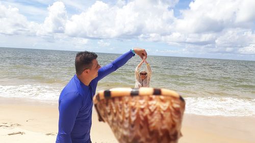 Optical illusion of man removing woman from shell at beach against sky