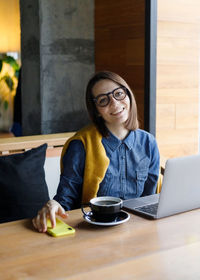 Young woman using mobile phone while sitting on table