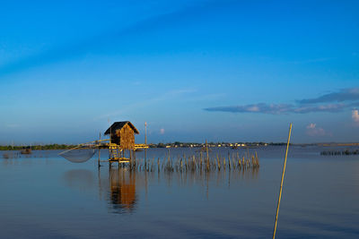 Wooden posts in lake against blue sky