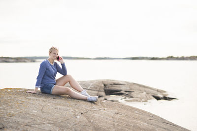 Woman sitting at sea and talking via cell phone