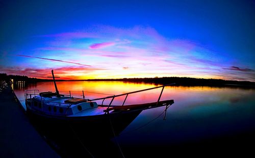 Sailboats moored in sea against sky during sunset