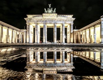 Brandenburg gate reflecting in puddle on street against sky at night