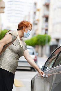 Side view of woman wearing flu mask standing by car in city