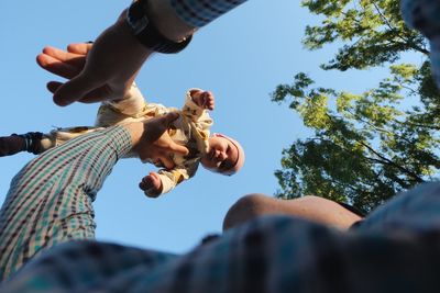Low angle view of father lifting baby against clear sky