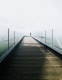 Woman standing on footbridge against sky