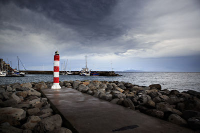 Lighthouse by sea against cloudy sky