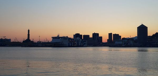 Sea by buildings against clear sky during sunset