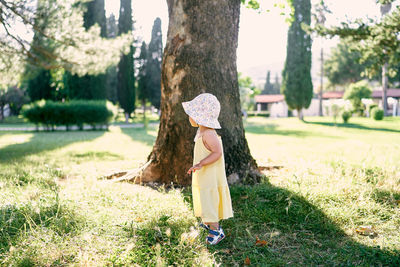 Woman standing by tree trunk on field