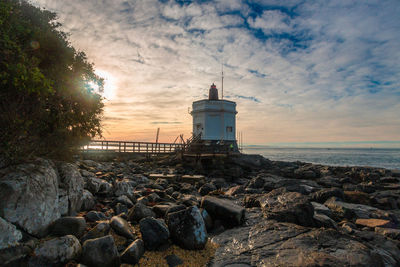 Lighthouse by sea against sky during sunset