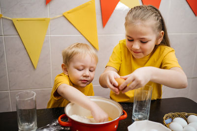 Girl breaks an egg into dough, brother helps cook, easter holiday