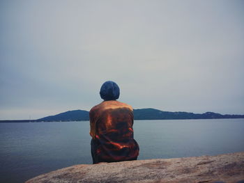 Rear view of man sitting in front of lake