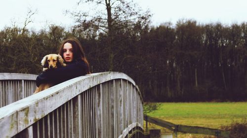 Portrait of young woman with dog on railing against trees