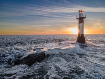 Lighthouse by sea against sky during sunset