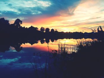 Silhouette trees by lake against sky during sunset