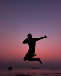 Silhouette man with arms raised standing against sky during sunset