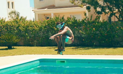 Full length of young man with skateboard jumping in swimming pool