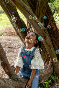 Happy girl looking away while sitting on tree trunk