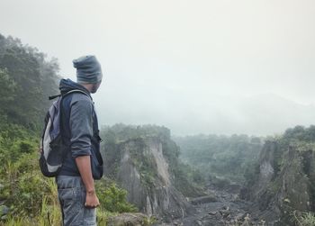 Rear view of man standing on mountain against sky