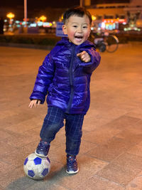 Full length portrait of boy playing soccer on street in city at night
