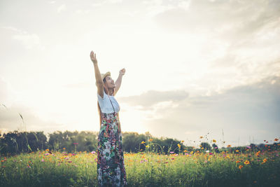 Young woman with arms raised standing against sky on field