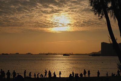 Silhouette people on beach against sky during sunset