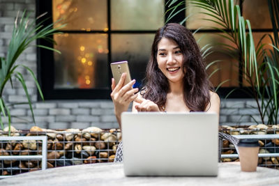 Smiling young woman using phone at cafe