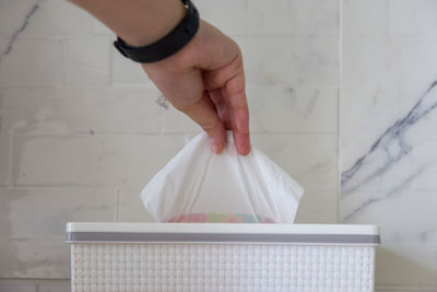 Cropped hand picking tissue paper from box against wall