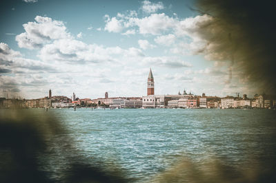 Buildings by river against cloudy sky