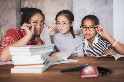 Portrait of smiling friends by books on table