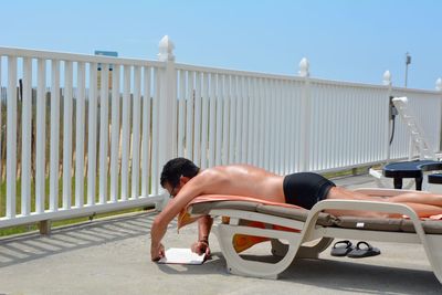 Full length of shirtless man lying on railing against sky