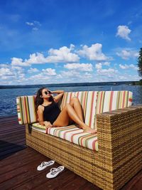 Teenage girl relaxing on sofa by sea against cloudy sky