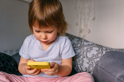 A small child at home on the couch uses a smartphone