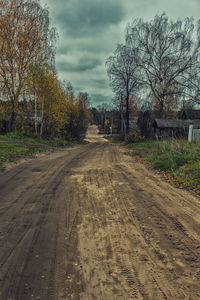 Dirt road amidst trees against sky