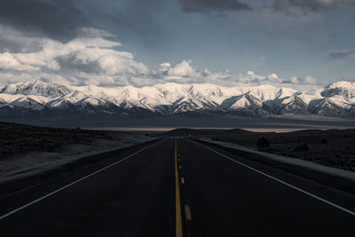 Empty road leading towards snowcapped mountains against sky