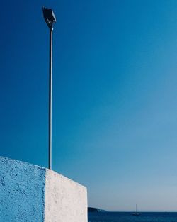 Low angle view of street light by sea against clear blue sky