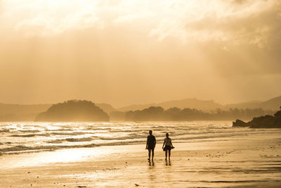 Silhouette people on beach against sky during sunset