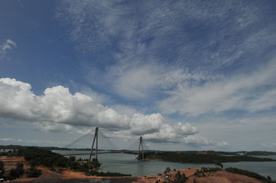 Suspension bridge over sea against cloudy sky