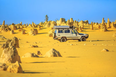 Yellow car on desert land against clear blue sky