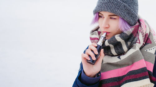 Close-up of young woman smoking while standing on snow covered field against sky