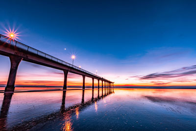 Illuminated pier over sea against sky during sunrise 