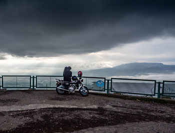 Man riding bicycle by railing against sky