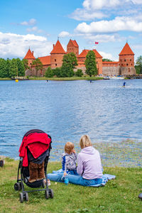 Rear view of people sitting on shore against sky